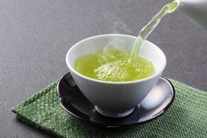 Фотография в чашку наливают зеленый чай из чайника. Биологический состав зеленого чая может улучшить функции мозга и сделать вас умнее